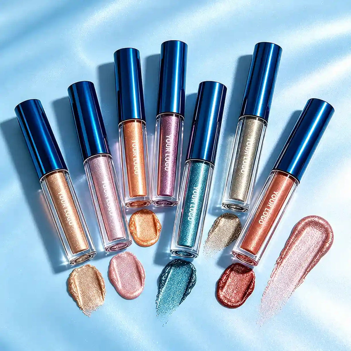 Custom liquid highlighters in clear tubes with metallic blue caps, shown with gold, pink, bronze and teal shimmer swatches.