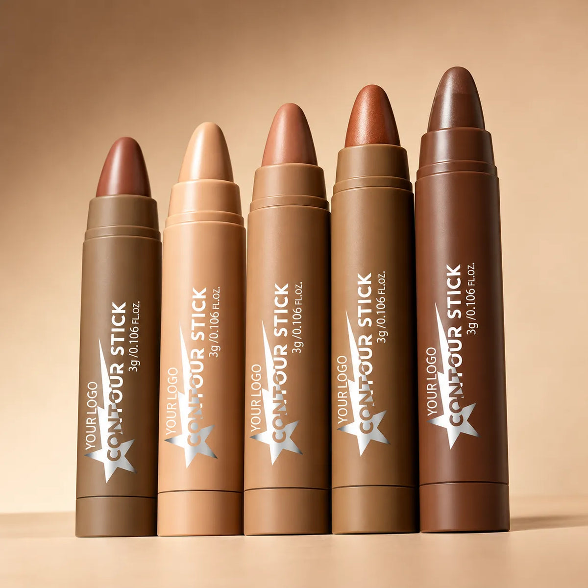 Five highlighter sticks in beige and bronze-toned tubes, displayed from light champagne to deep brown shades.