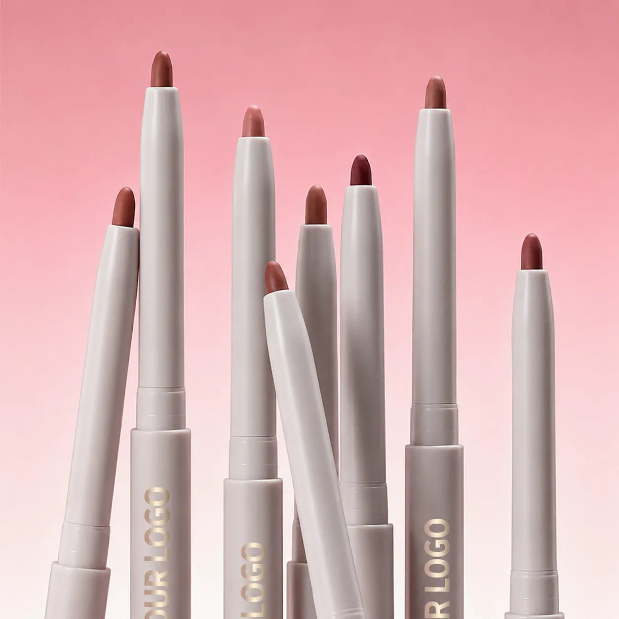 White lip liner pencils with exposed nude, pink and brown tips standing against a pink background.
