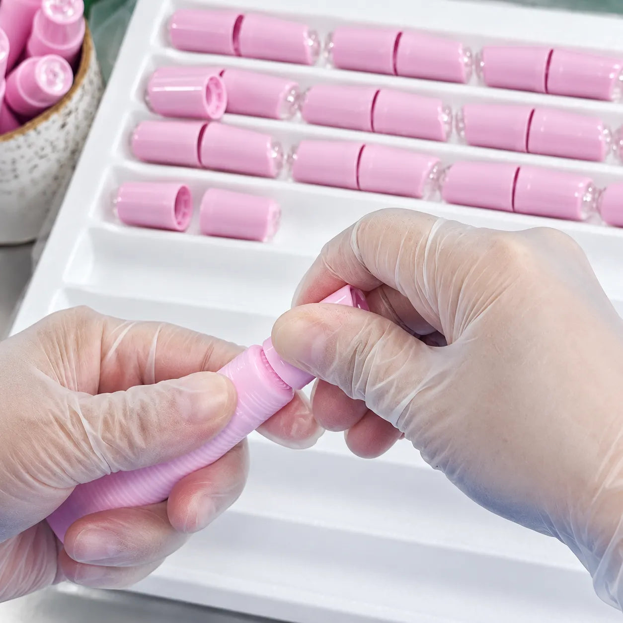 A gloved operator assembling and securing a pink lip oil container during production at KAIYA.