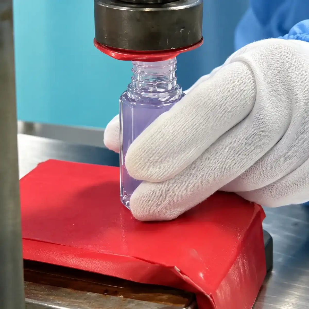 A gloved operator positioning a filled lip plumper container under production equipment at KAIYA.