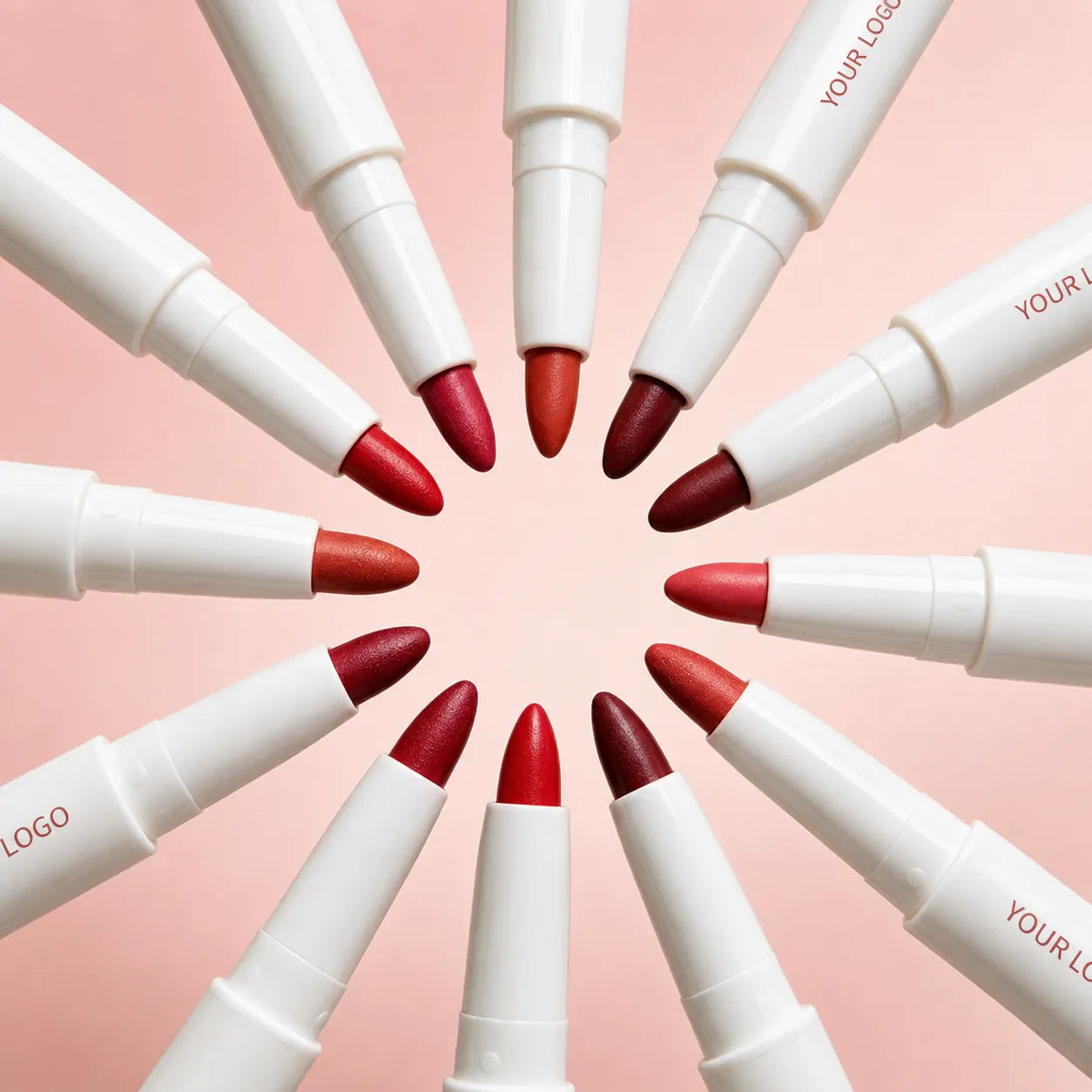 White liquid lip liner pens with red, brown and burgundy tips arranged in a circle on a pink background.