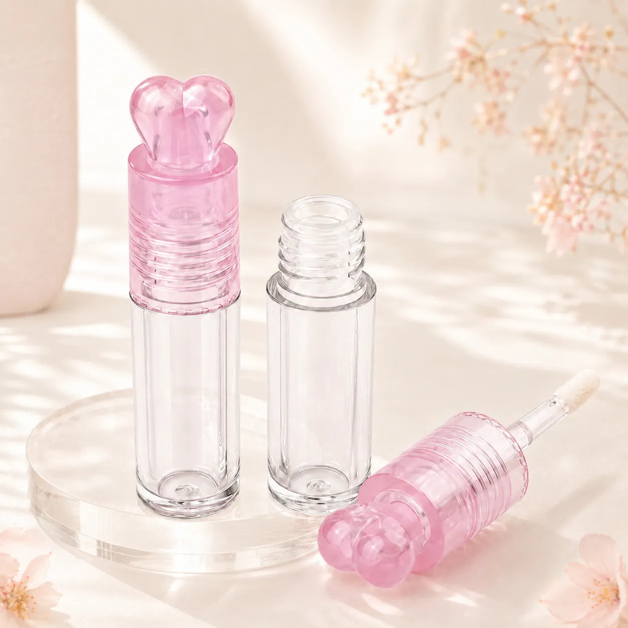 Clear lip gloss tube packaging with a pink heart-shaped cap and transparent bottle design.