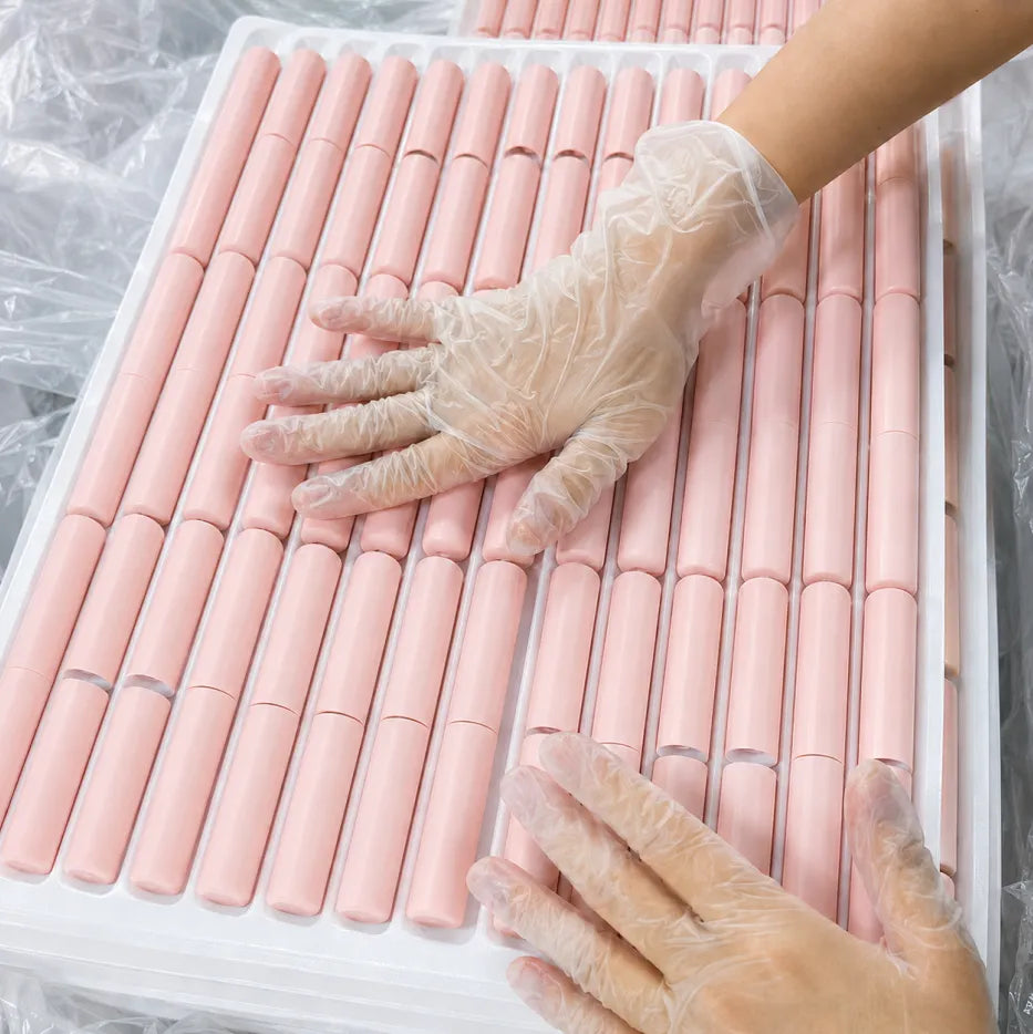 Custom cosmetic packaging by KAIYA, featuring pink empty cosmetic tubes arranged in trays during production inspection.