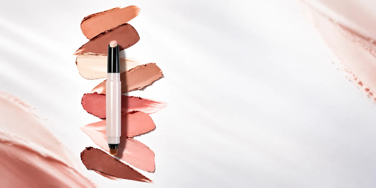 KAIYA custom eyeshadow stick with a built-in blending brush, displayed over cream color swatches in peach, rose and brown.