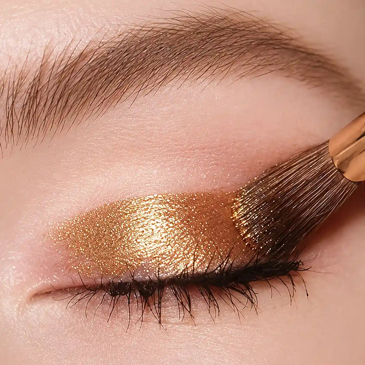 A brush spreading KAIYA gold shimmer eyeshadow across the eyelid in a close-up application view.