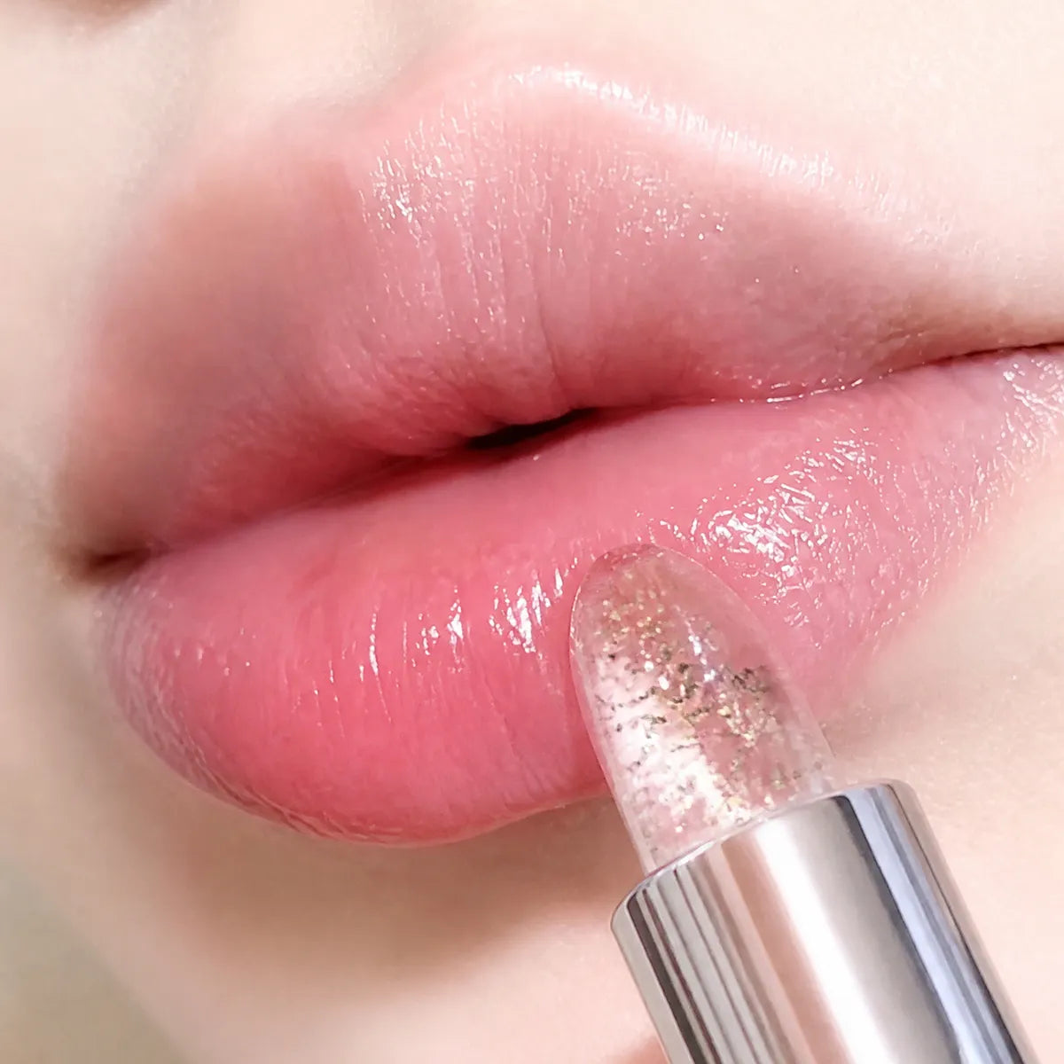 Close-up of foil color-changing lip balm with gold and silver flakes and a soft pink finish.