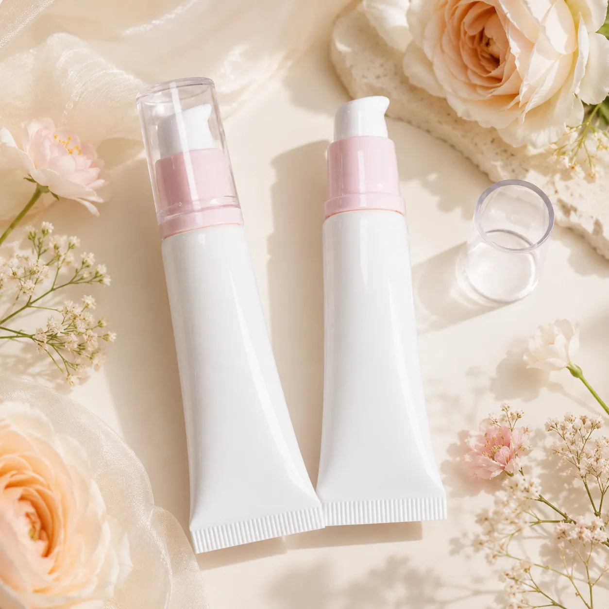 Lip gloss containers by KAIYA, featuring white lip gloss tubes with soft pink pump details in a floral display.
