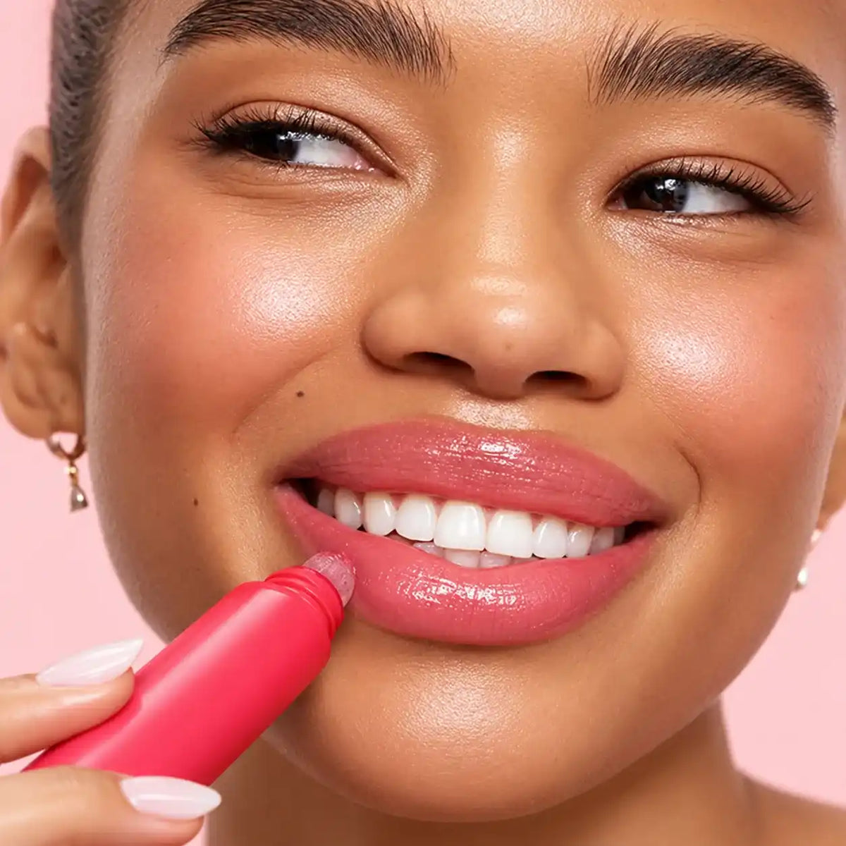 Model applying a lip plumper from a pink tube to lips with a glossy rosy finish.