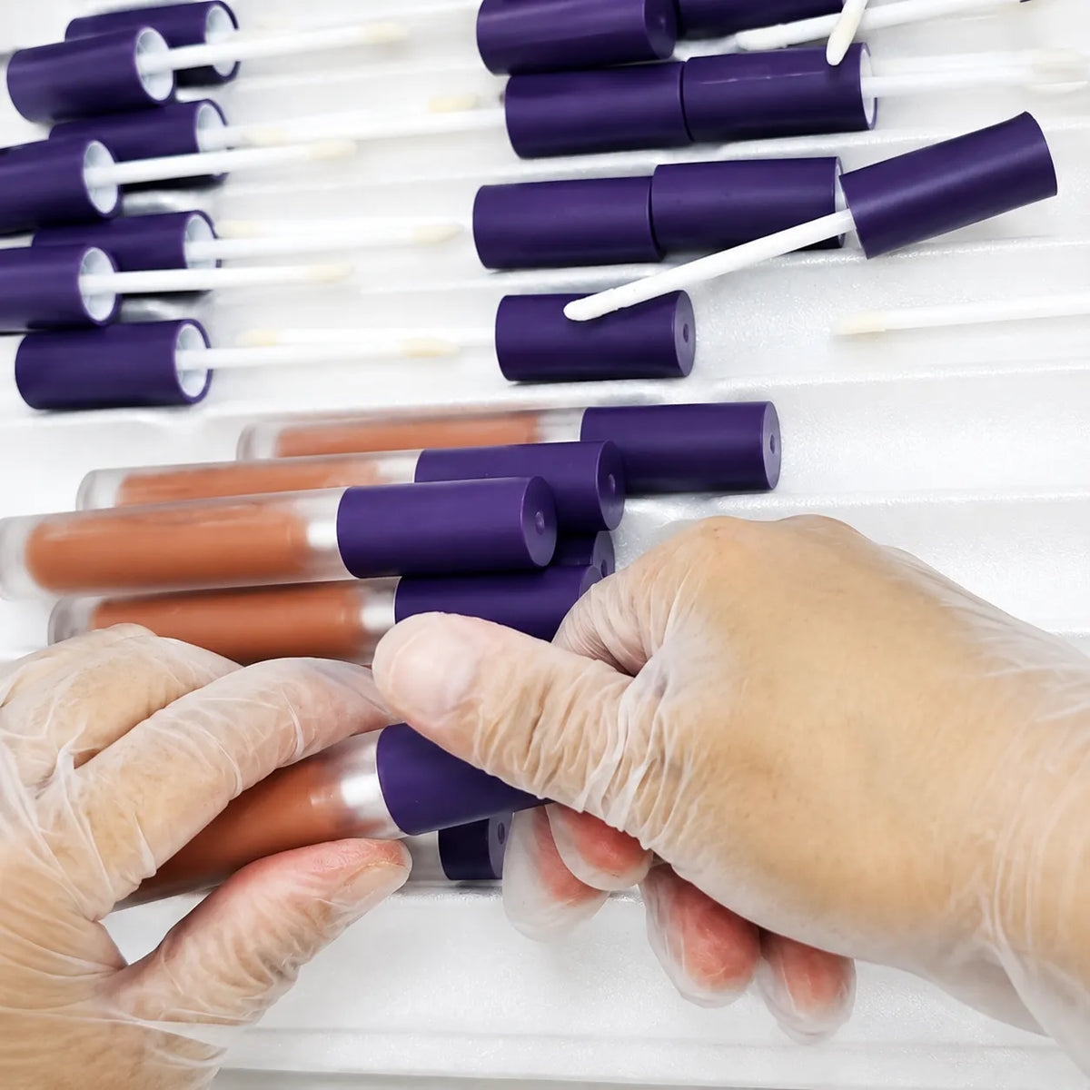 Workers inspecting and assembling liquid lipstick tubes, wands and caps during production