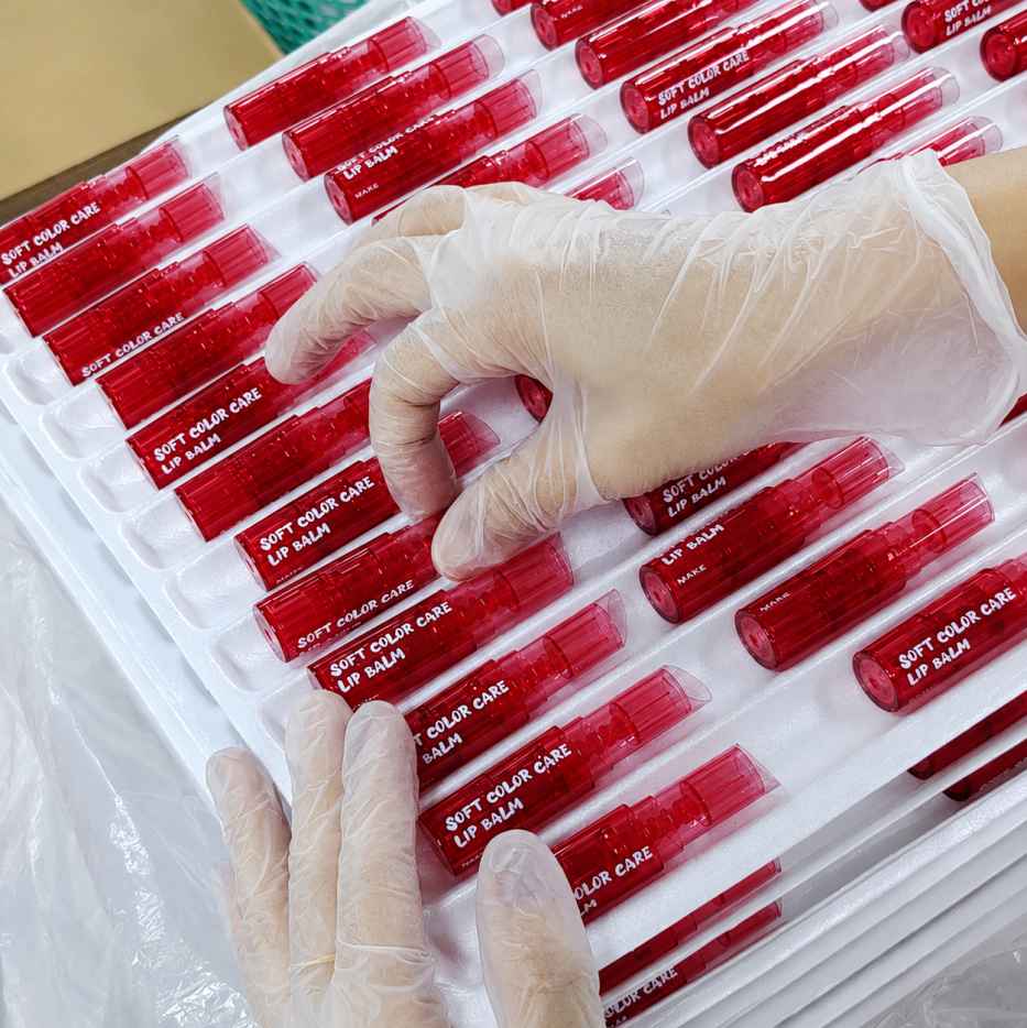 Private label cosmetic containers by KAIYA, featuring red empty lip balm tubes arranged in production trays for packaging inspection.