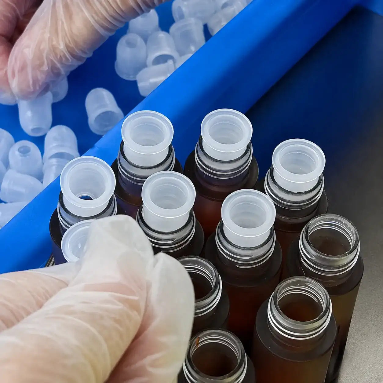 Gloved worker fitting wiper inserts into private label liquid lipstick tubes during assembly