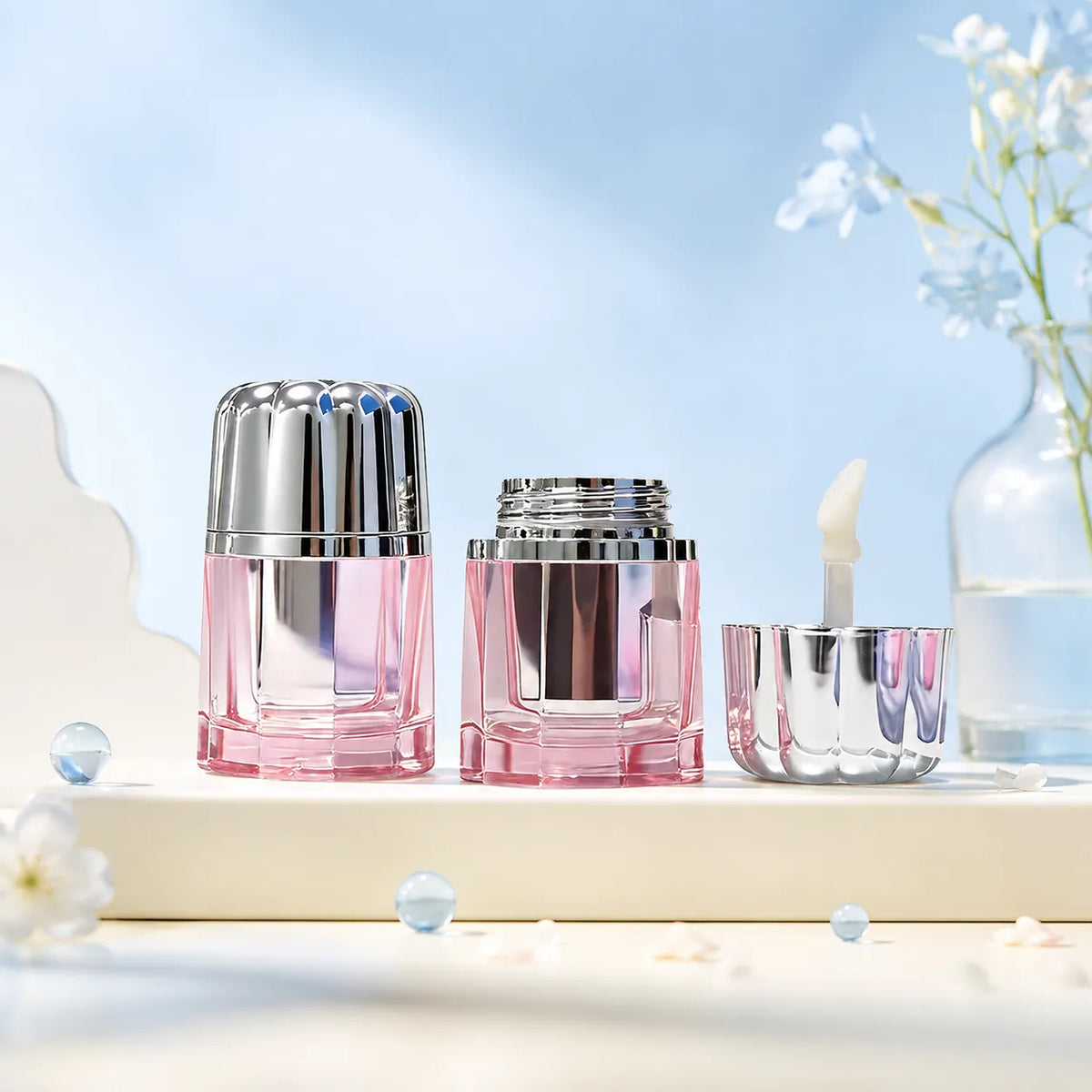 Small lip gloss containers in pink with silver caps and applicator, featuring compact cosmetic packaging design for custom lip gloss products.